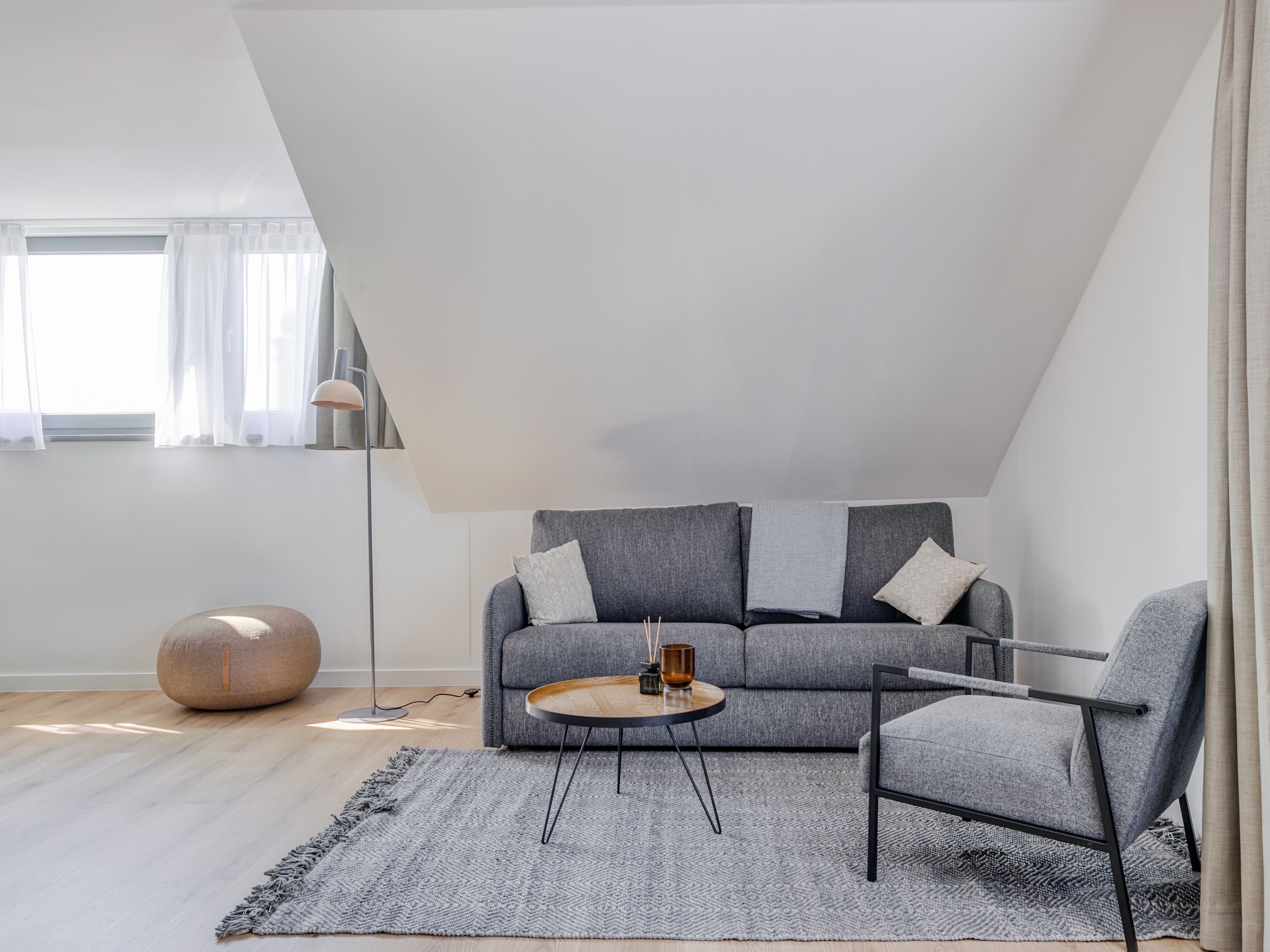 A modern living room with a gray sofa, a round coffee table, and a side chair. A floor lamp and a round table with a candle are also visible.