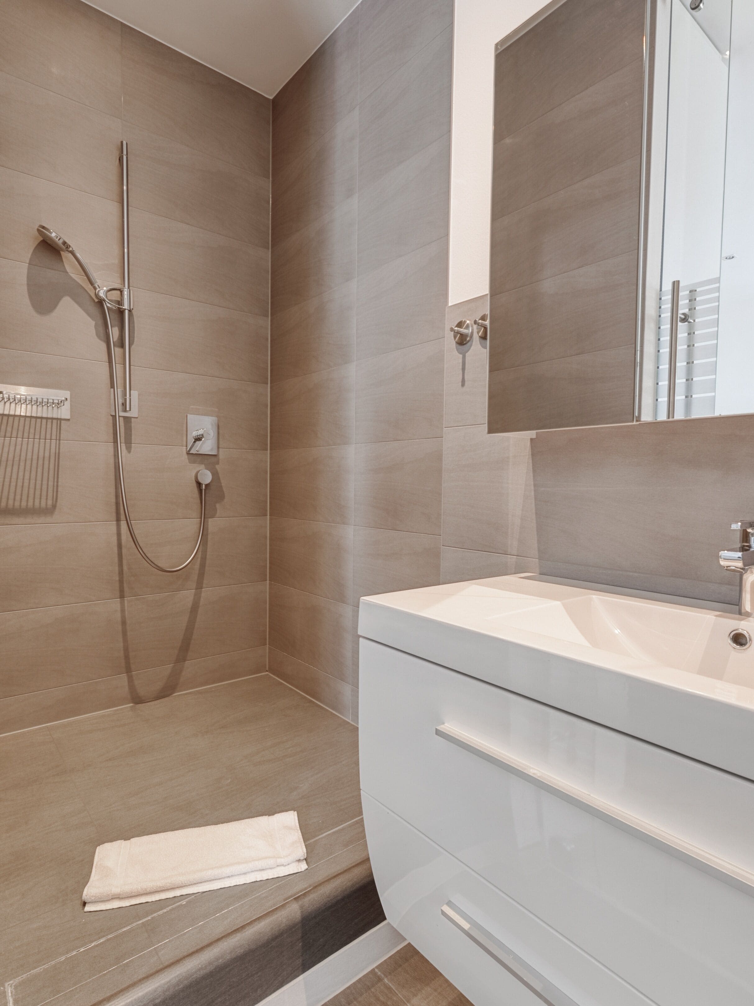 Een moderne badkamer met een inloopdouche, een grote spiegel en een wit wastafelmeubel.