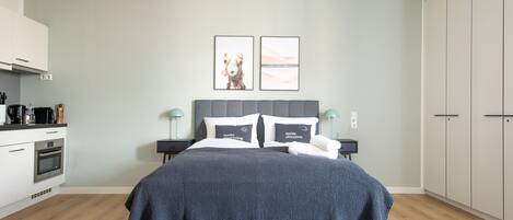 Un dormitorio moderno con una cama gris, dos mesitas de noche, un cabecero gris y un armario amplio.