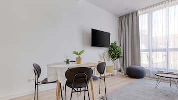 En moderne stue med spiseplads, et fladskærms-TV og store vinduer med gardiner.