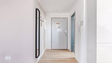 Un corridoio moderno e luminoso con pavimento in legno, pareti bianche e una porta in fondo.