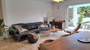 A modern living room with a leather sofa, a wooden dining table, and a large window offering a view of the outdoors. - EXCEPTIONAL IN THE COUNTRYSIDE 15mn from BIARRITZ (Saint Pierre d'Irube)