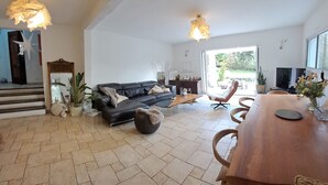 A spacious living area with a black leather sofa, a wooden dining table, and a large window offering a view of the outdoors. - EXCEPTIONAL IN THE COUNTRYSIDE 15mn from BIARRITZ (Saint Pierre d'Irube)