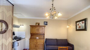 Un espace de vie compact comprenant un coin cuisine, un espace repas avec une table et des chaises, un canapé et un lustre décoratif.