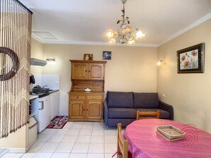 A compact living space with a kitchenette, a dining area with a table and chairs, a sofa, and a decorative chandelier.