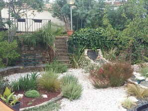 A garden with a variety of plants, a stone wall, and a metal gate.