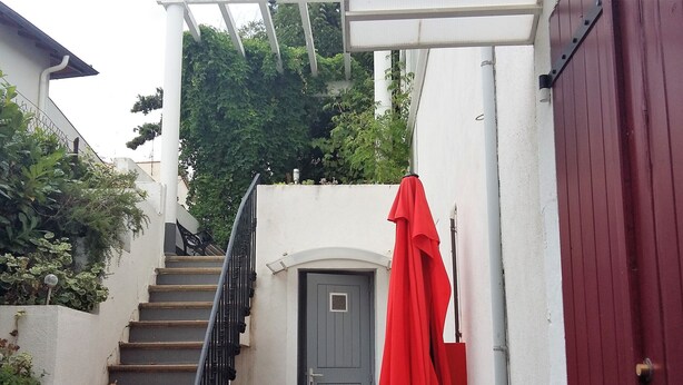 Un escalier étroit mène à une porte, à côté de laquelle est accroché un parapluie rouge.