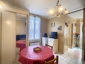 A room with a dining table, a computer desk, a chair, a window with curtains, a radiator, and a decorative light fixture.