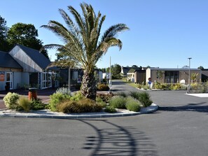 A hotel with a palm tree in the center, a parking lot, and a building with a sign that reads 'BUREAU DE VENTE.' - Luxury Mobile Home, 3BR, Near Beach, Heated Pool, Gym, WiFi (Jullouville)