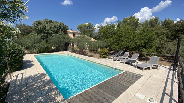 A rectangular swimming pool with clear blue water, surrounded by a wooden deck and stone tiles.