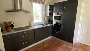 A kitchen with dark cabinets, a stainless steel range hood, a built-in oven, and a window with a view of trees.