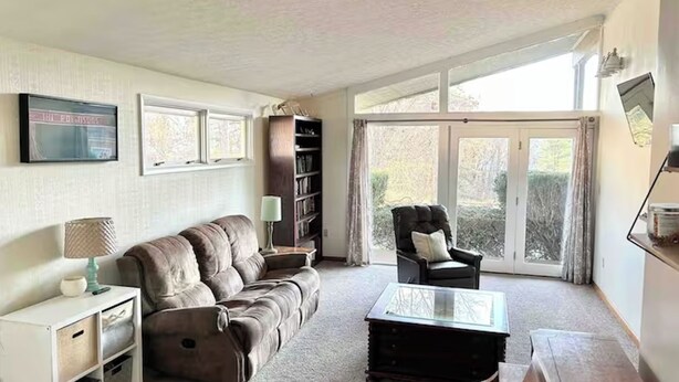 A living room with a sofa, armchair, and a glass-top coffee table. There is a bookshelf and a lamp on a side table. - Cheerful 3 BR Residential Home in Small Town USA (woodsfield)