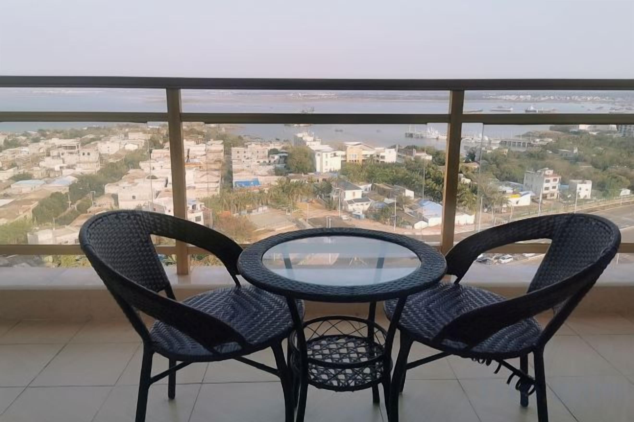 Un balcón con vistas a un paisaje urbano, con dos sillas de mimbre y una pequeña mesa redonda.