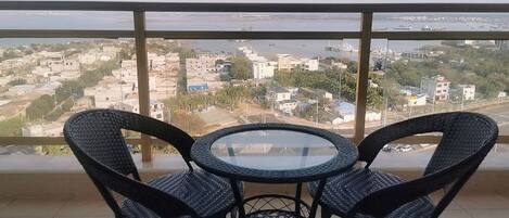 A balcony with a view of a cityscape, featuring two wicker chairs and a small round table.
