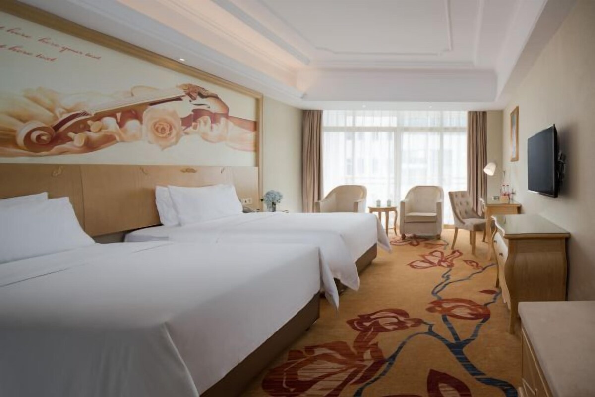 Habitación de hotel con dos camas, un ventanal grande, televisor de pantalla plana y alfombra estampada.