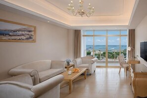 Un salón moderno con un conjunto de sofás, una mesa de centro, un televisor y un ventanal con vistas al mar.