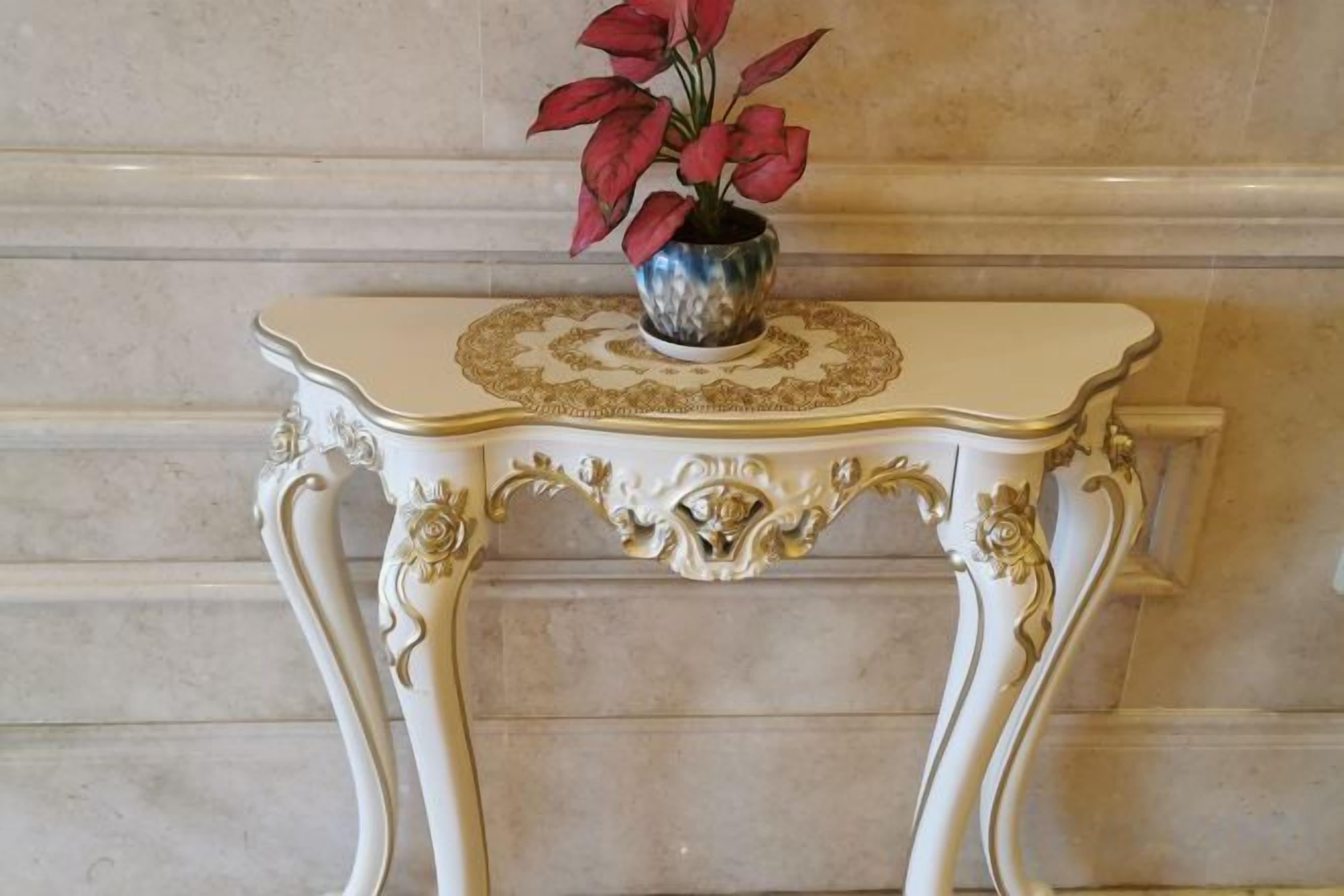 A white ornate table with a decorative top and a vase with red flowers.
