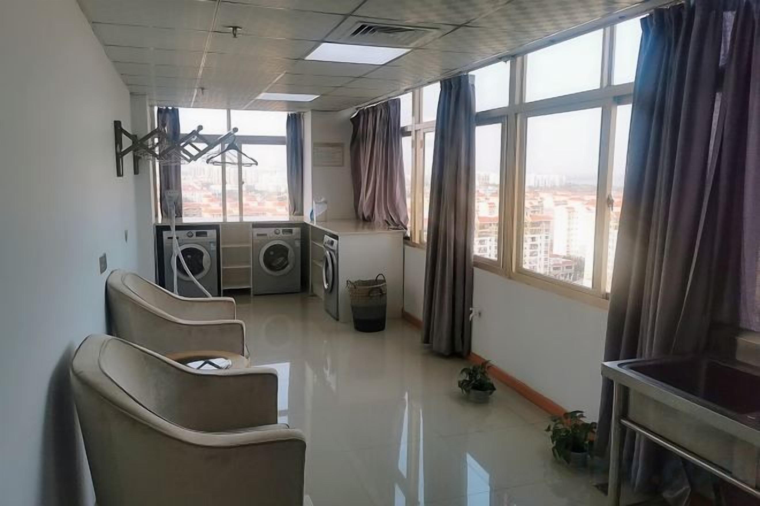 A hotel room with a view, a washing machine, a chair, and a small table.
