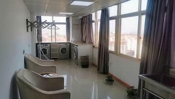 A hotel room with a view, a washing machine, a chair, and a small table.