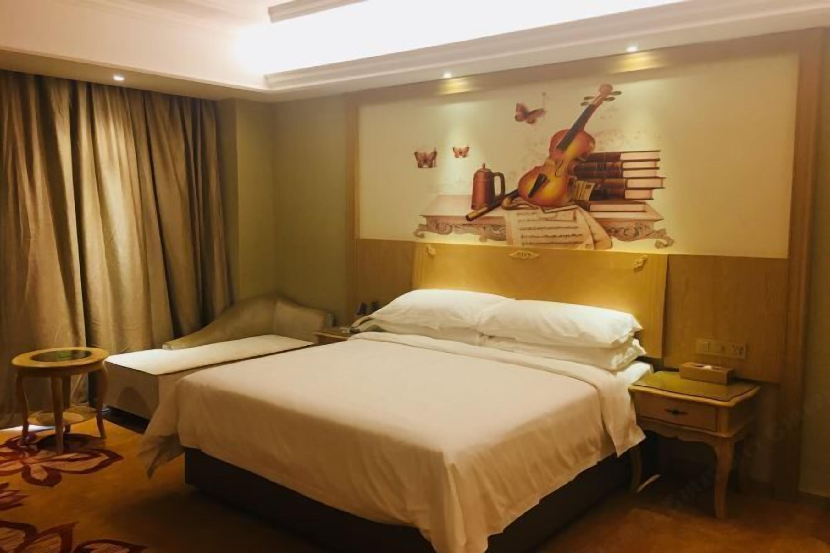 Ett hotellrum med en stor säng, ett sängbord, en stol, ett litet runt bord och en väggmålning som föreställer en gitarr och böcker.