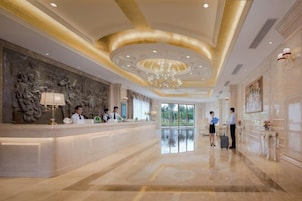 A hotel lobby with a reception desk, a chandelier, and a large painting on the wall.