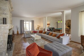 Un salon spacieux avec une cheminée, un ensemble de canapés, une table basse et un coin repas à l’arrière-plan.
