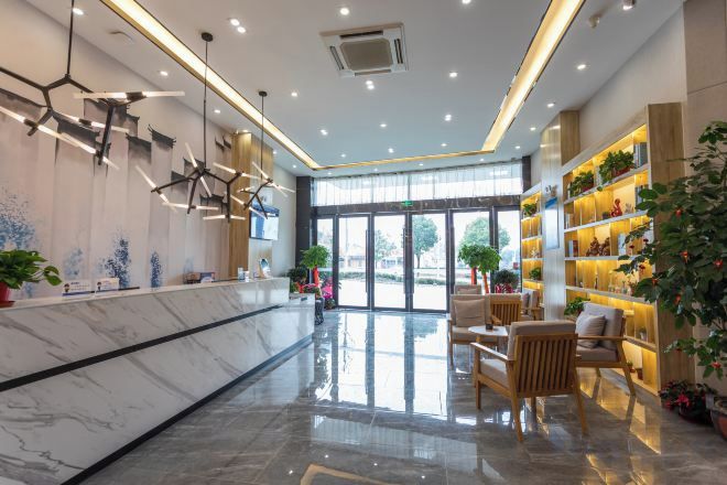 Un vestíbulo de hotel con un mostrador de recepción de mármol, luminarias modernas, asientos cómodos y un amplio ventanal con vistas al exterior.
