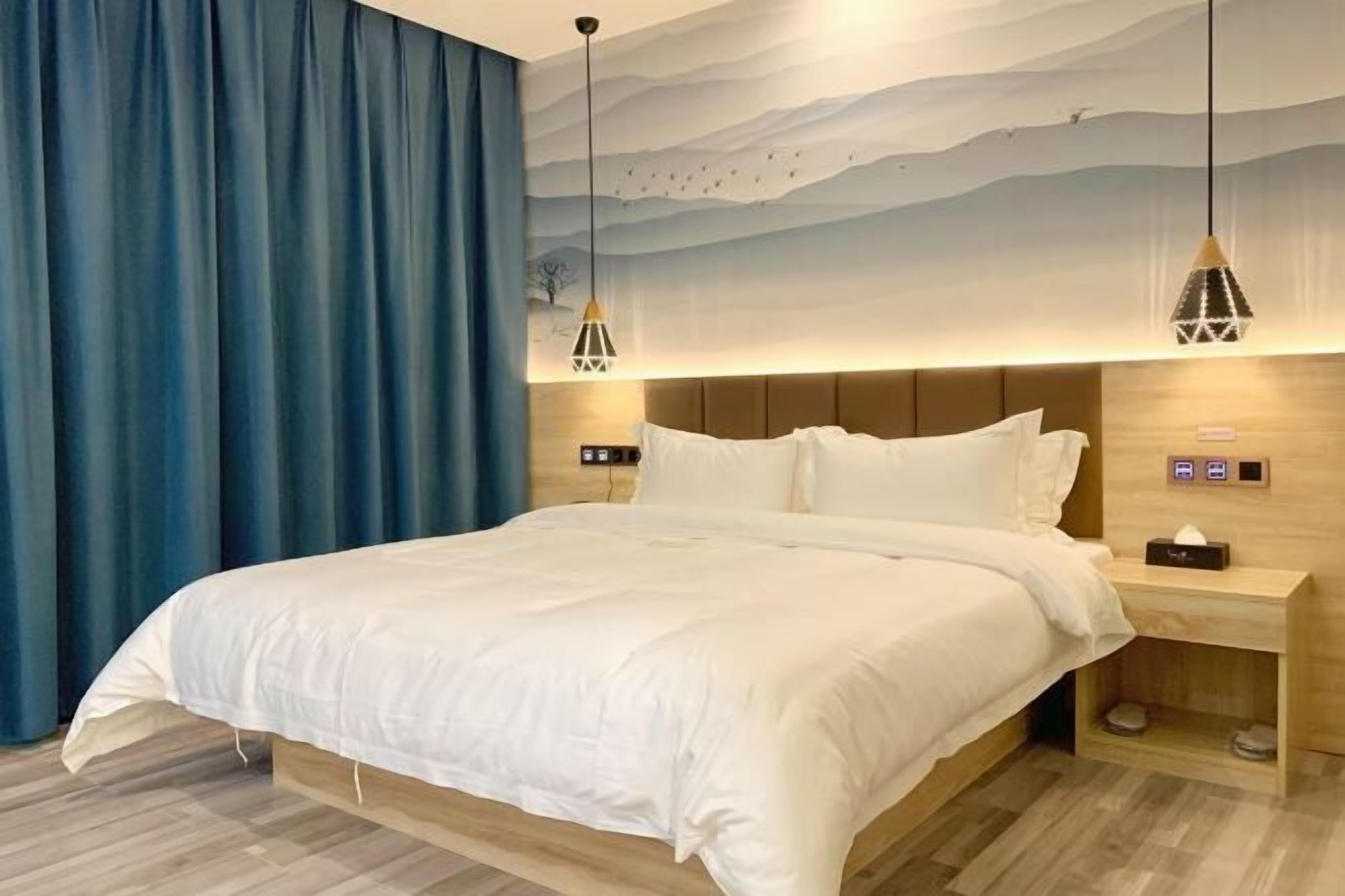 Quarto de hotel moderno com uma cama grande, cabeceira de madeira e uma mesa de cabeceira com abajur.