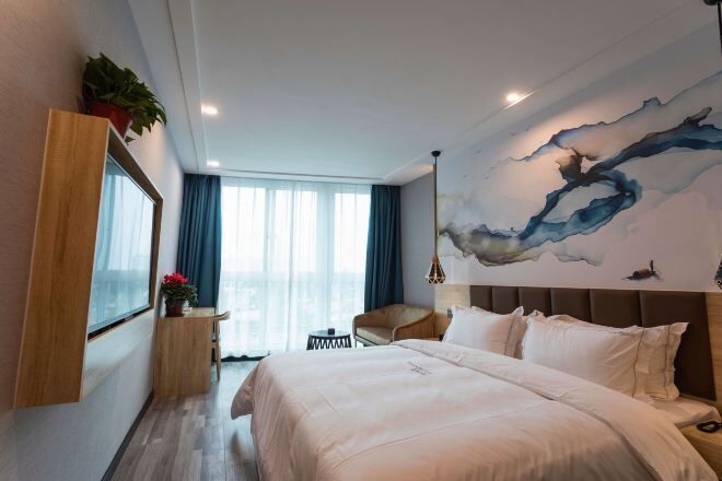 Quarto de hotel moderno com uma cama grande, uma escrivaninha e vista da cidade através de amplas janelas.