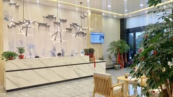 A hotel reception area with a marble counter, modern pendant lights, and a television screen.