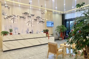 Un espace d’accueil d’hôtel avec un comptoir en marbre, des luminaires suspendus modernes et un écran de télévision.