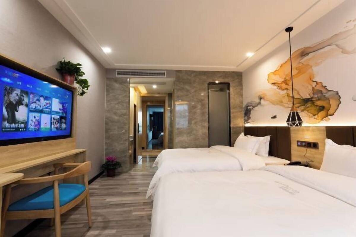 A hotel room with a bed, a TV mounted on the wall, a desk with a chair, and a large abstract painting on the wall.