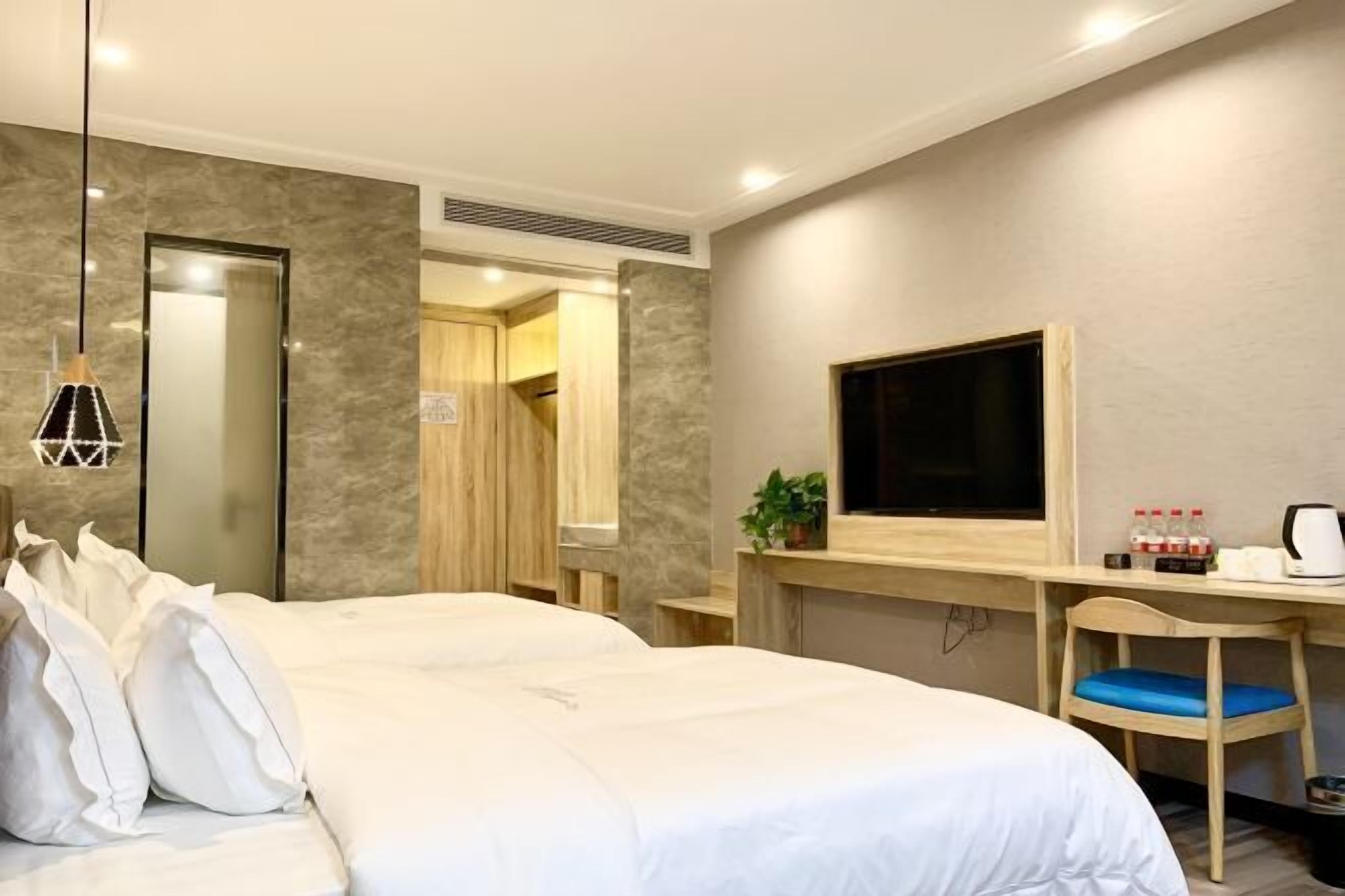 Quarto de hotel com uma cama grande, uma escrivaninha com televisão de tela plana, uma cadeira e uma pequena planta.