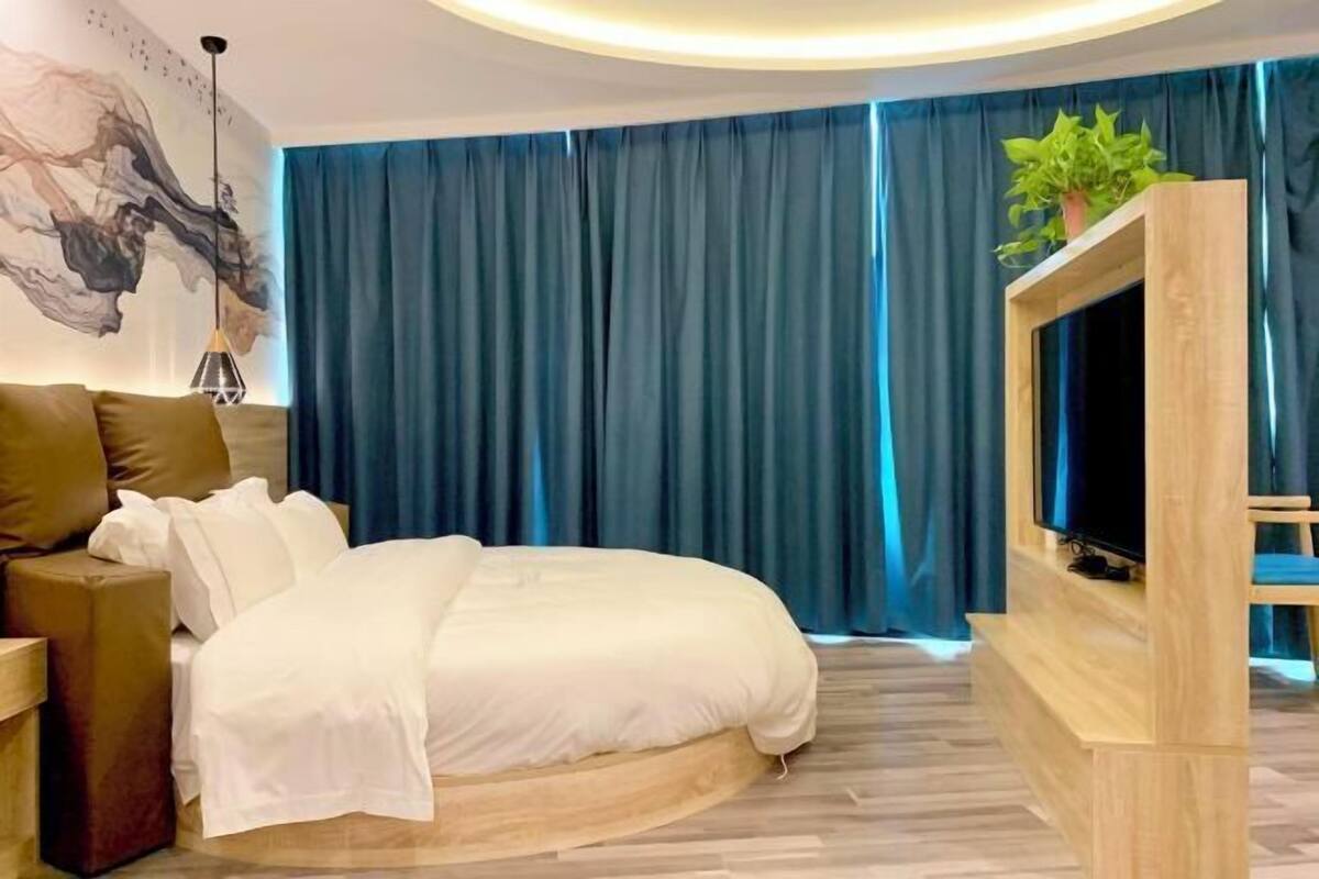 A modern bedroom with a bed, a TV, and a large window with curtains.