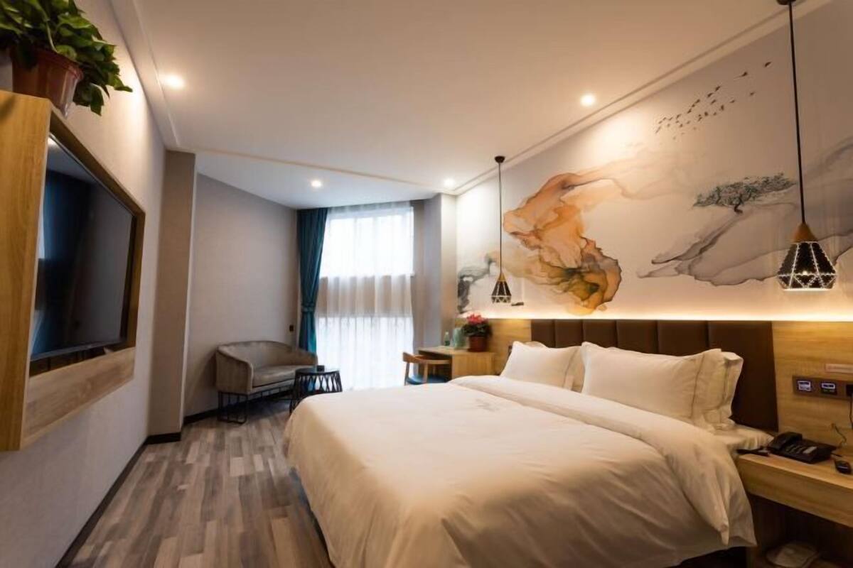 A hotel room with a large bed, a desk, a chair, a TV, and a wall with a painting.