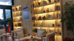 A cozy seating area with wooden chairs and tables, surrounded by shelves with books and decorative items. - Qingmu Select Hotel (Jintan No.4 Middle School Yaoban Branch) (Changzhou)