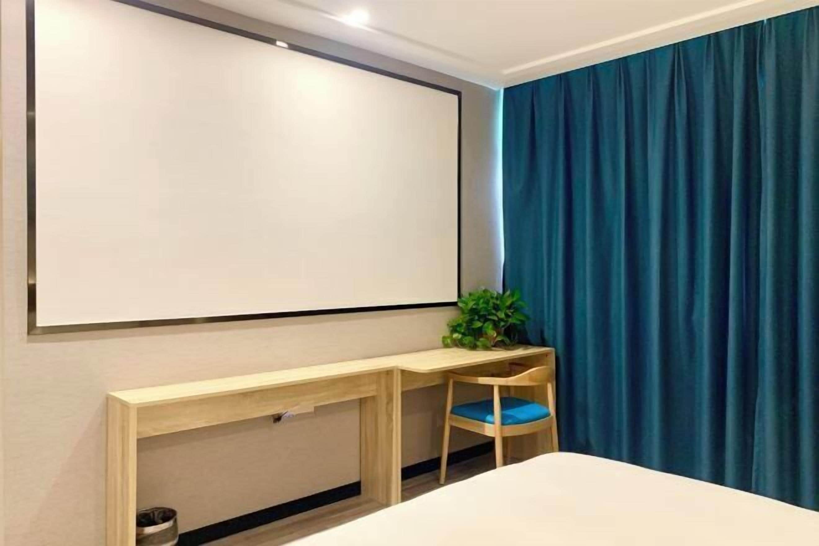 Una camera da letto con un letto, una scrivania, una sedia, una pianta e un'ampia finestra con tende.