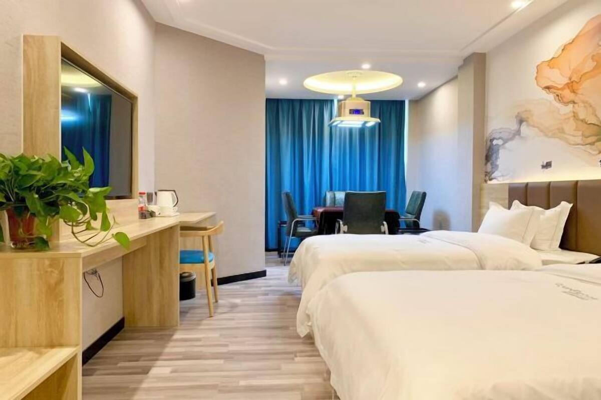 A hotel room with two beds, a desk with a chair, a large mirror, and a dining table with chairs.