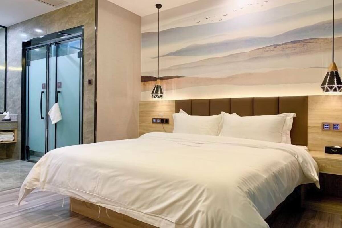 A modern hotel room with a large bed, a glass door entrance, and a mural on the wall.