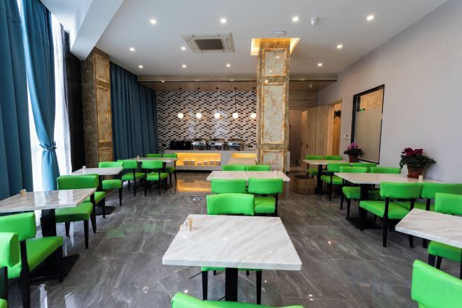 Un restaurante con sillas verdes y mesas blancas, una zona de bar y una pared con diseño.