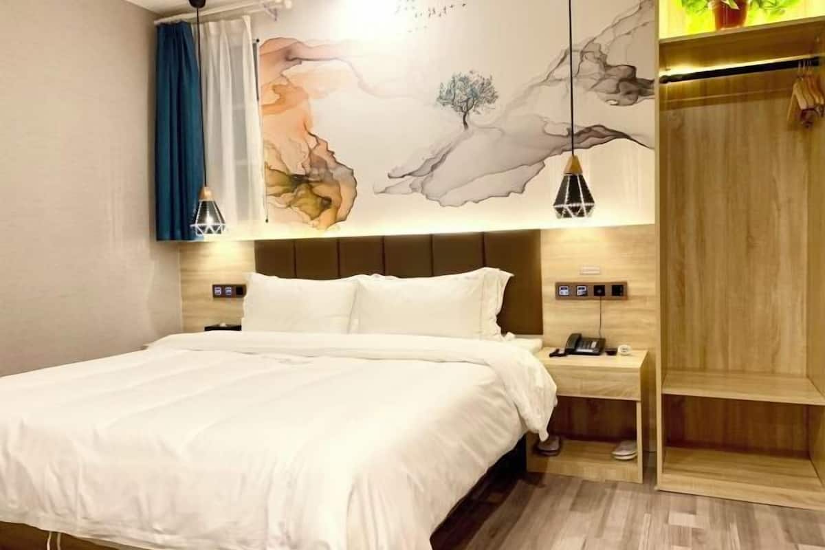 A bedroom with a bed, bedside tables, a wall-mounted phone, and a wooden wardrobe.
