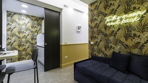 Una habitación con un sofá azul oscuro, una pequeña mesa con una silla y una zona de kitchenette.