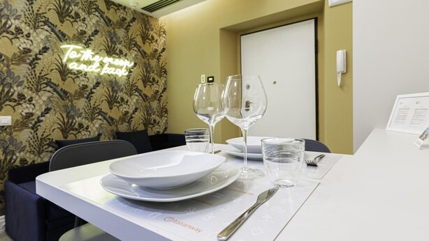 A dining area with a table set for two, featuring plates, glasses, and cutlery. A neon sign on the wall reads "To the moon and back." - Italianway Collection - Corso Venezia 7 - Tosca (Milan)