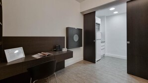 A modern hotel room with a dark wood desk, a black chair, a framed picture on the wall, and a white door leading to a kitchen area. - Italianway Collection - Corso Venezia 7 - Tosca (Milan)