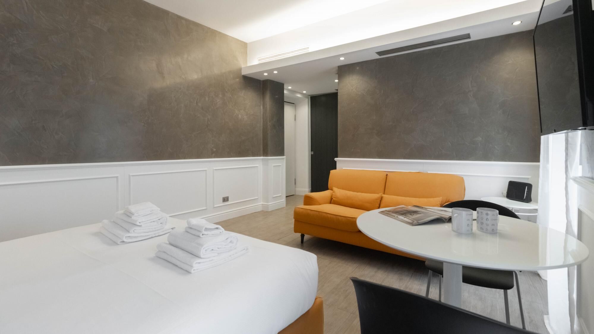 Una habitación de hotel moderna con una cama grande, una mesa redonda, un sofá y un televisor.