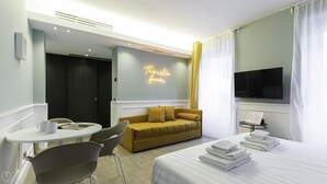 Una habitación de hotel con cama, sofá, mesa de comedor con sillas, televisor y un letrero de neón en la pared.