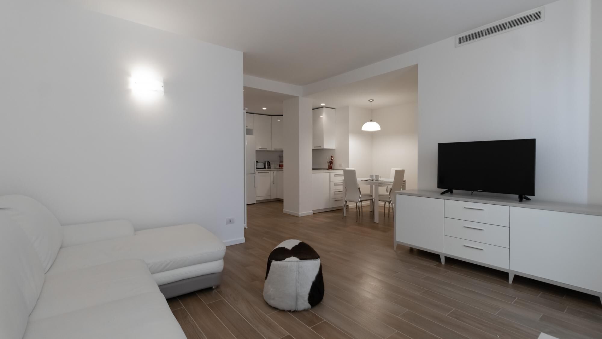 Una sala moderna con sofá, televisor y comedor con sillas y mesa.