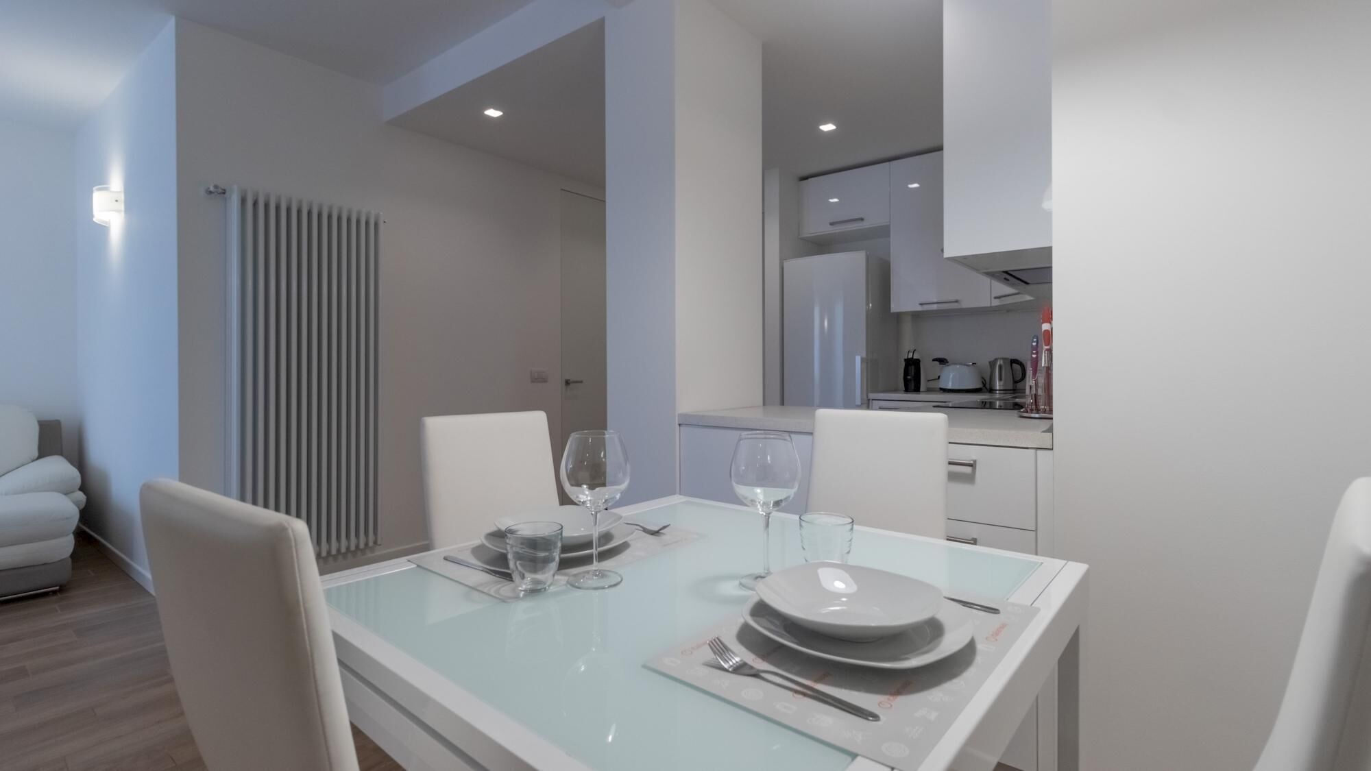 Un comedor moderno con una mesa de vidrio, sillas blancas y vistas a la cocina.