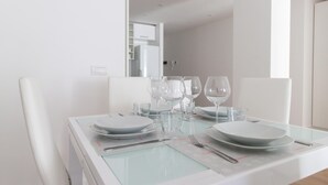 Une table à manger dressée avec des assiettes, des verres et des couverts, dotée d’un plateau en verre et de chaises blanches.
