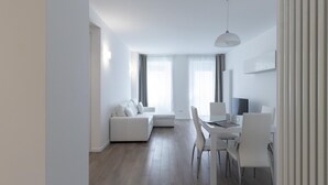 Un salon moderne et minimaliste, avec un canapé blanc, une table à manger et des chaises, ainsi qu’un téléviseur à écran plat.